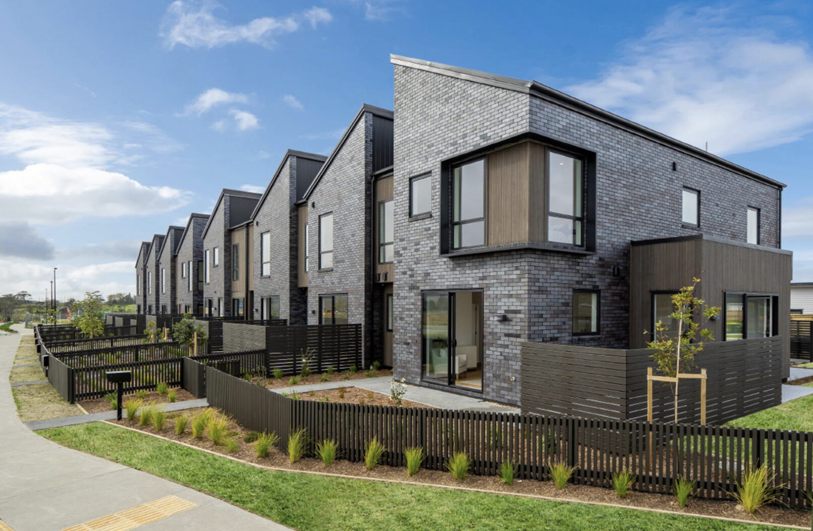 An exterior shot of the row of townhouses, featuring the front fencing and landscaping.
