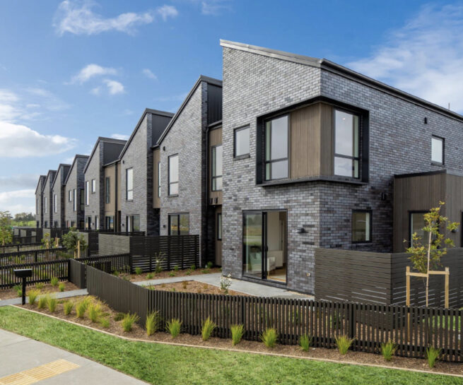 An exterior shot of the row of townhouses, featuring the front fencing and landscaping.
